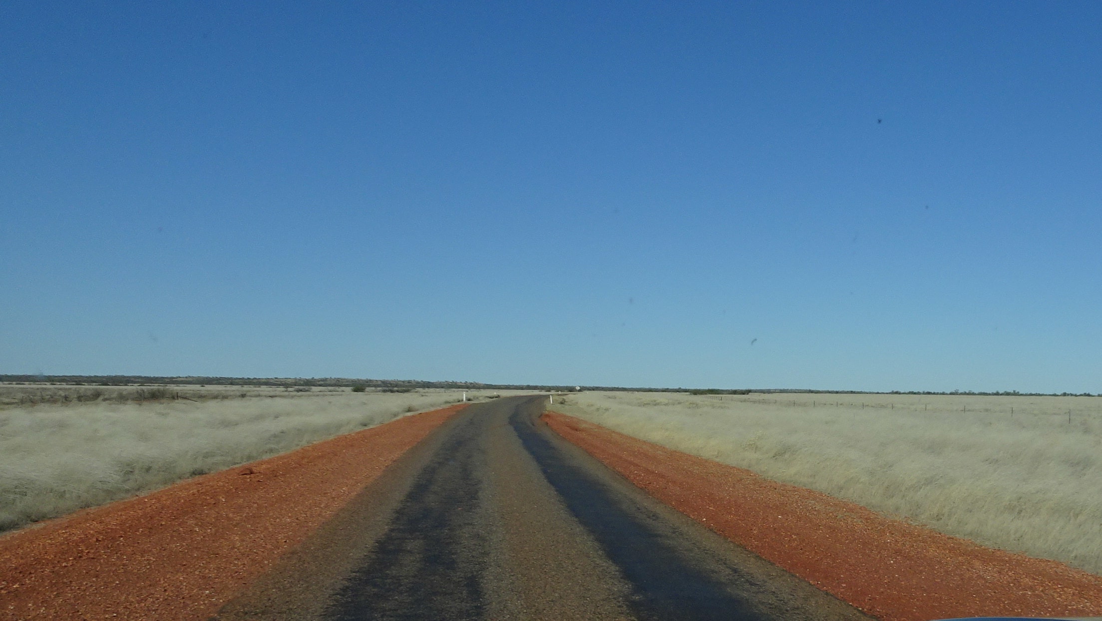 Desolate one-lane outback highway surrounded by white grassy plains