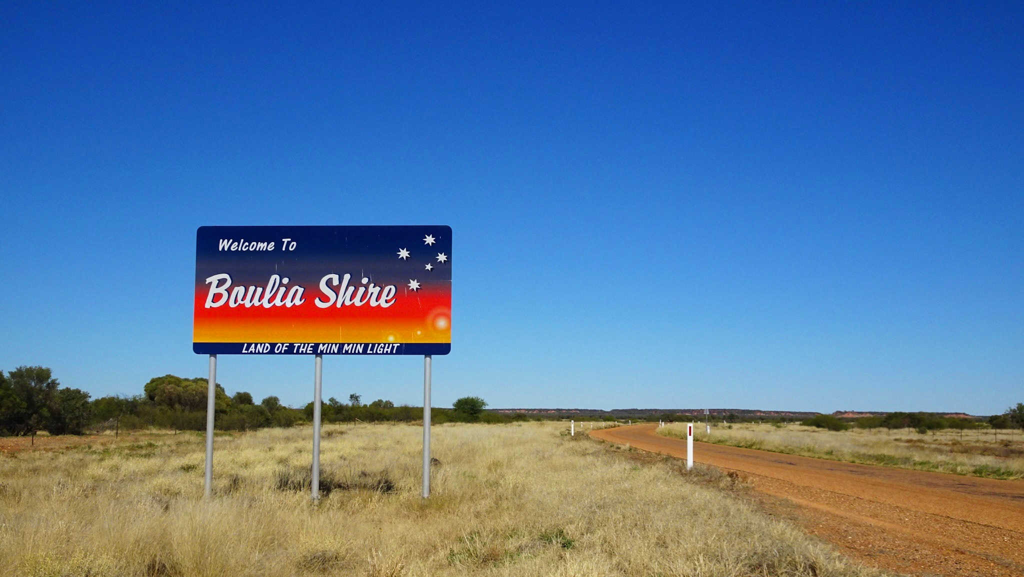 Welcome to Boulia Shire sign by red dirt road 