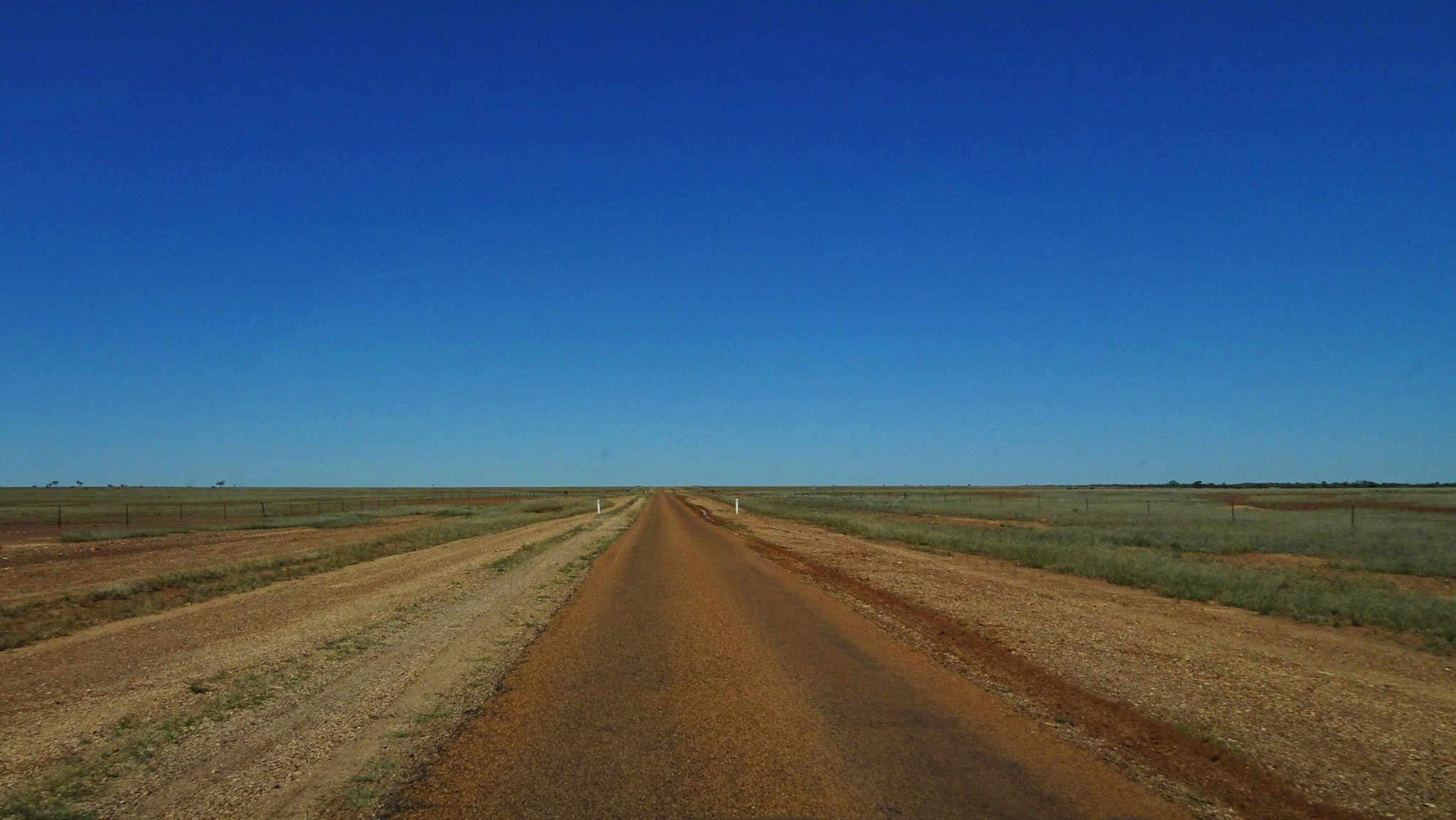 Desolate outback one-lane highway under blue sky