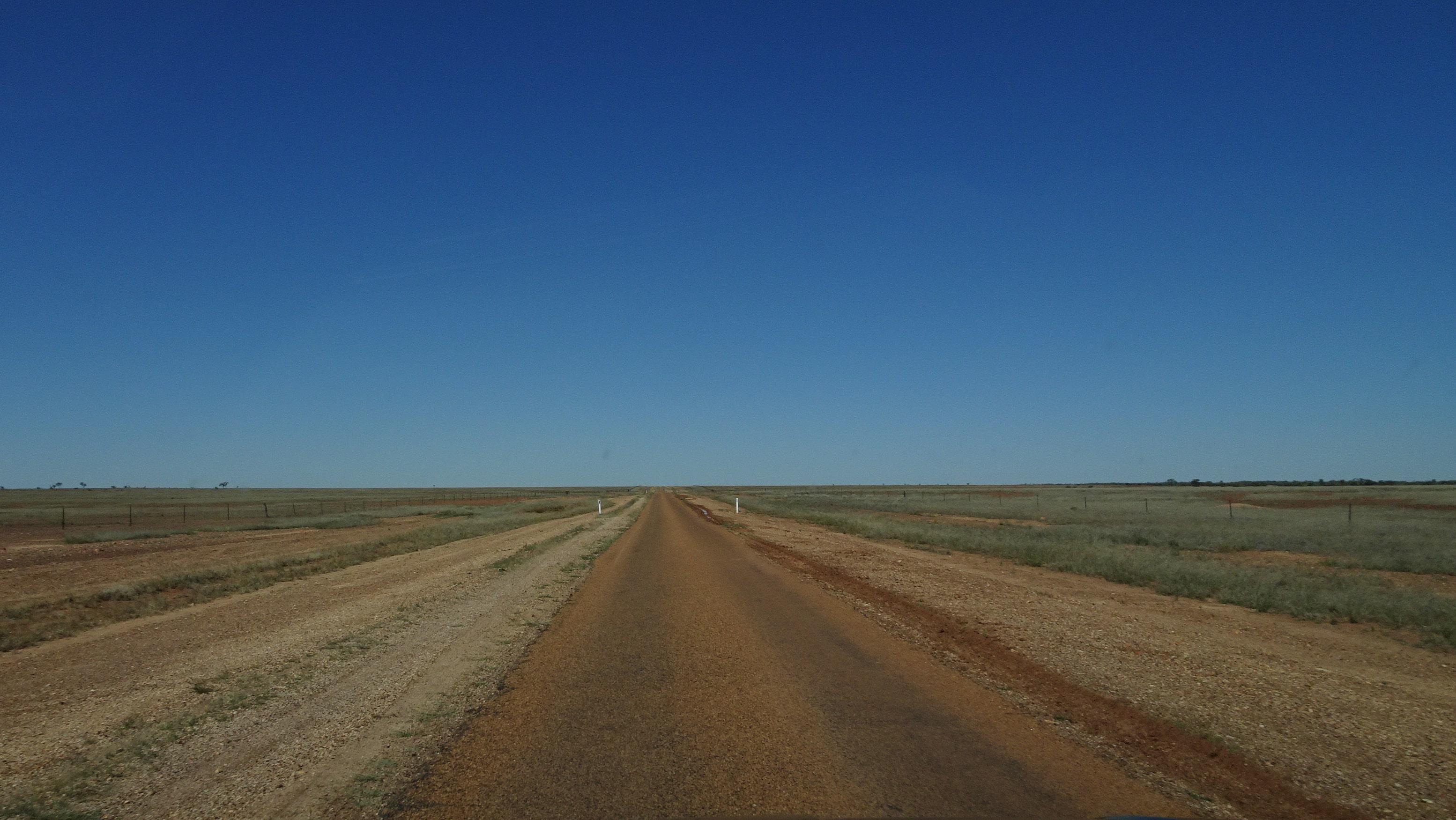 Desolate outback one-lane highway under blue sky